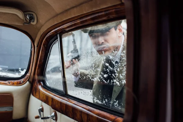 Enfoque selectivo de mafioso con pistola mirando dentro de coche retro - foto de stock