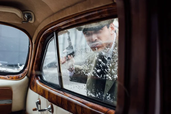 Enfoque selectivo de mafioso con pistola mirando dentro de coche retro — Stock Photo