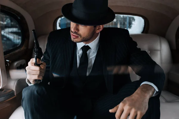 Selective focus of gangster sitting with revolver in retro car — Stock Photo