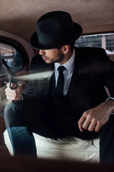 Selective focus of gangster in black suit and felt hat with gun in retro car — Stock Photo