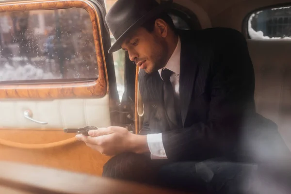 Mafioso guardando revolver in mano mentre seduto in auto — Foto stock