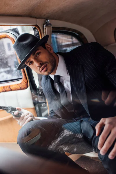 Selective focus of gangster with gun looking at camera and sitting in car — Stock Photo