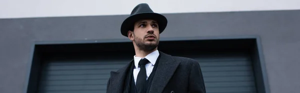 Vista de ângulo baixo de mafioso em casaco preto e chapéu com arma na rua, tiro panorâmico — Fotografia de Stock