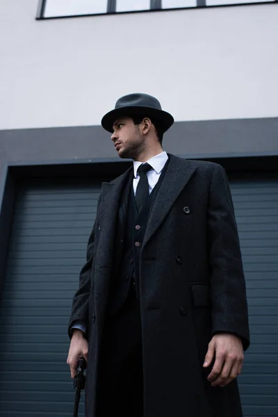 Vue en angle bas du gangster en manteau noir et chapeau avec revolver regardant loin sur la rue — Photo de stock