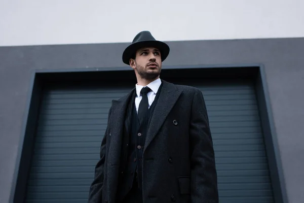 Low angle view of mafioso in black coat and felt hat on street — Stock Photo