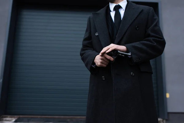 Vista ritagliata di gangster in cappotto nero che tiene revolver sulla strada — Foto stock