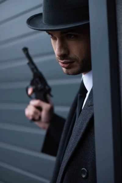 Selective focus of mafioso with gun in corner near wall on street — Stock Photo