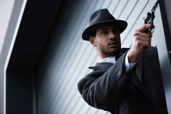 Low angle view of mafioso aiming gun with outstretched hand from corner on street — Stock Photo