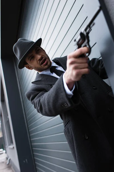 Selective focus of mafioso aiming weapon with outstretched hand from corner on street — Stock Photo