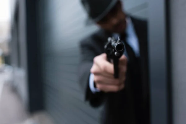 Selective focus of mafioso silhouette with outstretched hand aiming weapon from corner on street — Stock Photo