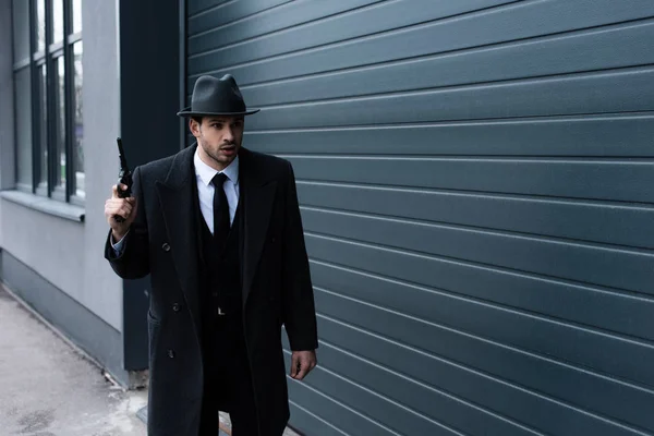 Selective focus of surprised mafioso with weapon near wall on street — Stock Photo