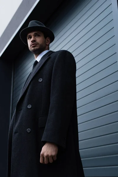Vista ad angolo basso del mafioso in elegante cappotto vicino alla parete sulla strada — Foto stock