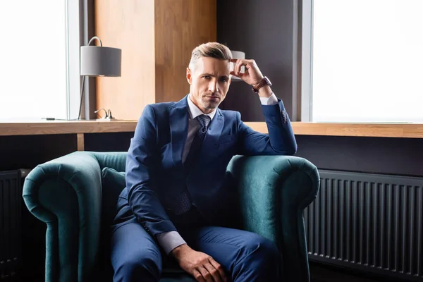 Businessman in suit sitting in armchair and looking at camera — Stock Photo