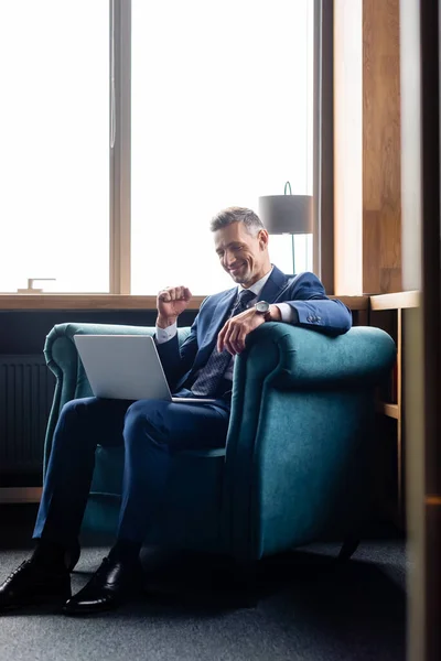 Sonriente hombre de negocios en traje mostrando sí gesto y el uso de la computadora portátil - foto de stock