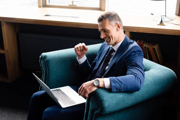 Vista de ángulo alto de hombre de negocios sonriente en traje que muestra sí gesto y el uso de la computadora portátil - foto de stock