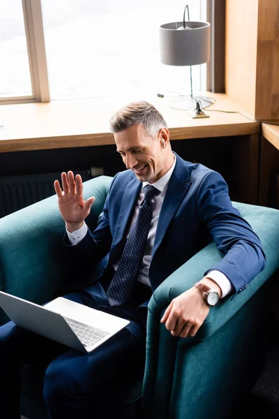 Vista de ángulo alto del hombre de negocios sonriente en traje ondeando durante la videollamada - foto de stock