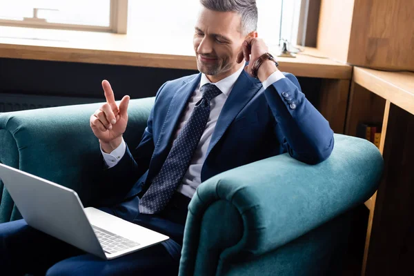 Hombre de negocios sonriente en traje usando el ordenador portátil y mostrando signo de idea - foto de stock