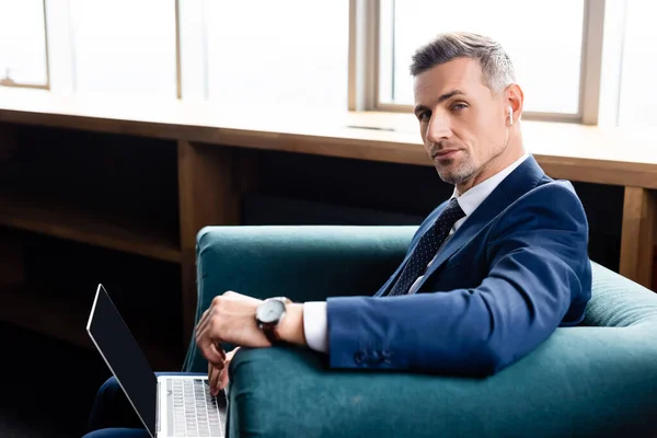 Businessman in suit with earphones and laptop looking at camera — Stock Photo