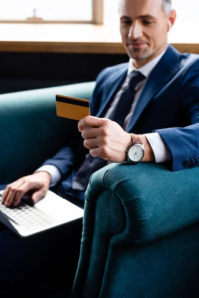 Enfoque selectivo de sonriente hombre de negocios en traje con tarjeta de crédito y el uso de ordenador portátil - foto de stock