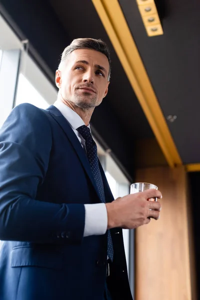 Vue à angle bas de bel homme d'affaires en costume tenant le verre — Photo de stock