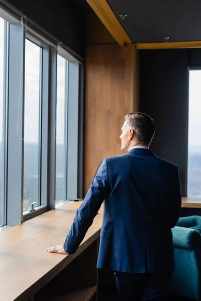 Rückansicht des Geschäftsmannes im Anzug, der durch das Fenster schaut — Stockfoto