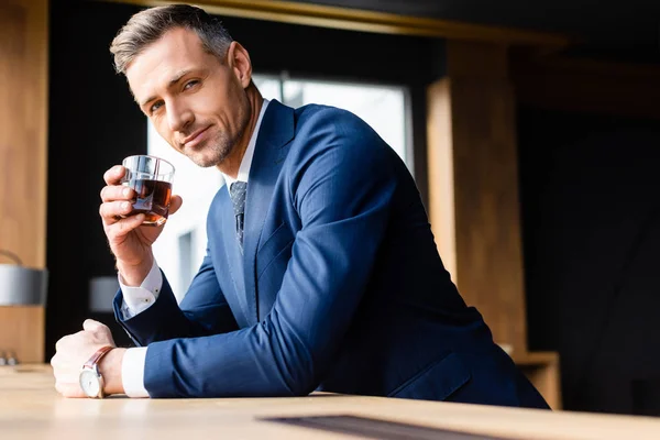 Hombre de negocios en traje sosteniendo vidrio y mirando a la cámara - foto de stock