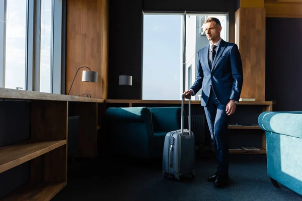 Handsome businessman in suit walking with travel bag in hotel — Stock Photo