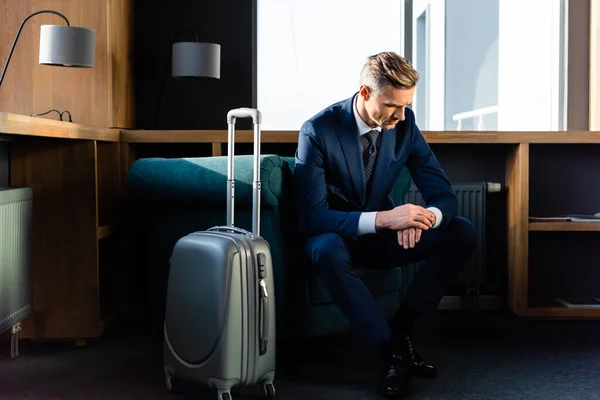 Homme d'affaires en costume assis près du fauteuil et regardant la montre-bracelet — Photo de stock