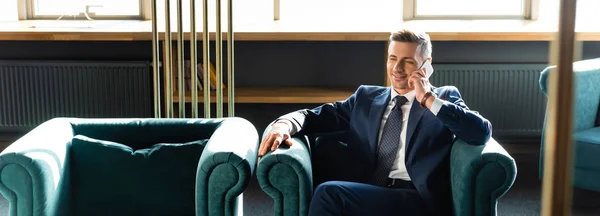 Colpo panoramico di uomo d'affari sorridente in giacca e cravatta che parla su smartphone — Foto stock