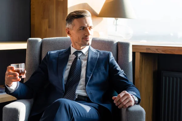 Smiling businessman in suit sitting in armchair and holding glass — Stock Photo