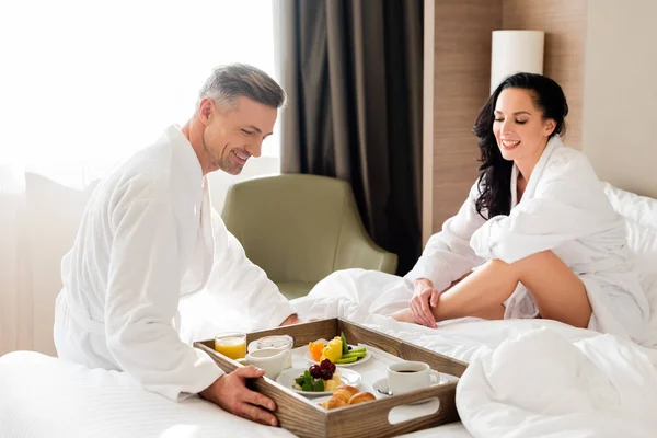 Novio trayendo el desayuno en la cama para sonreír novia en el hotel - foto de stock