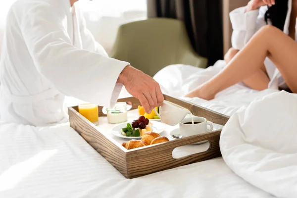 Abgeschnittene Ansicht von Freund, der Milch in Kaffee gießt und Freundin, die auf Bett sitzt — Stockfoto