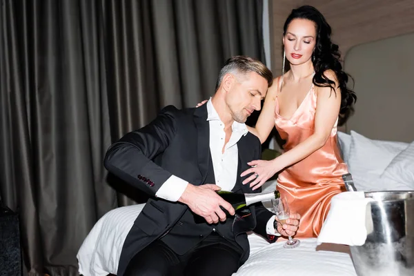 Freund schenkt Champagner ein und Freundin umarmt ihn im Hotel — Stockfoto