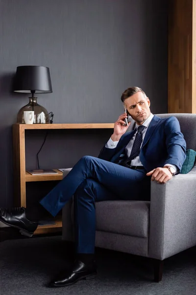 Businessman in suit talking on smartphone and sitting in armchair — Stock Photo