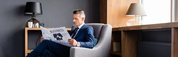 Панорамный снимок бизнесмена в костюме читающего газету с деловыми надписями — стоковое фото
