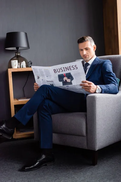 Hombre de negocios en traje leyendo periódico con letras de negocios y sentado en sillón - foto de stock