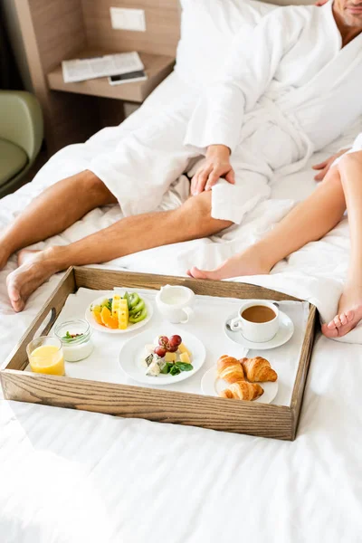 Cropped view of boyfriend and girlfriend in bathrobes sitting near tray with food — Stock Photo