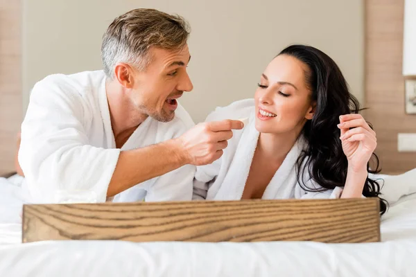Smiling boyfriend feeding attractive girlfriend with cheese in hotel — Stock Photo