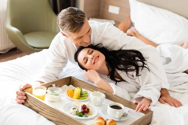 Handsome boyfriend hugging smiling girlfriend near tray with food — Stock Photo
