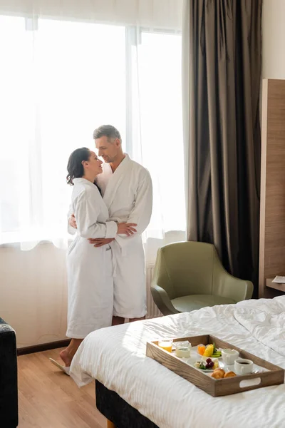 Vista lateral de novio y novia en albornoces abrazándose en el hotel - foto de stock