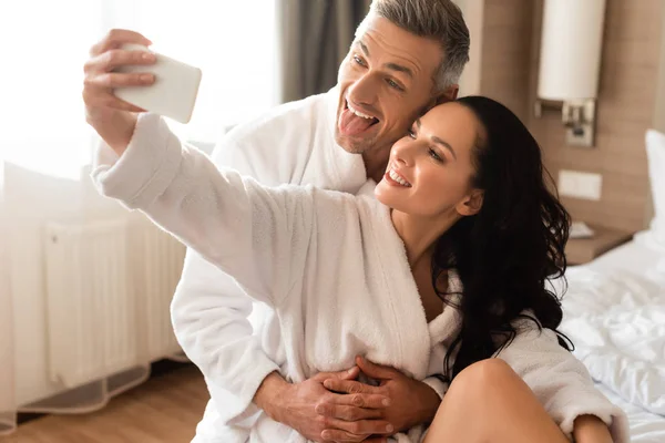 Novio sobresaliendo lengua y novia tomando selfie en hotel — Stock Photo