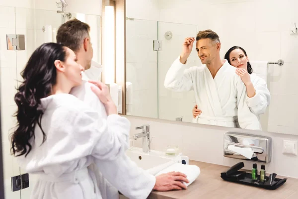 Enfoque selectivo de novio peinando el pelo y la novia sonriente abrazándolo en el hotel - foto de stock