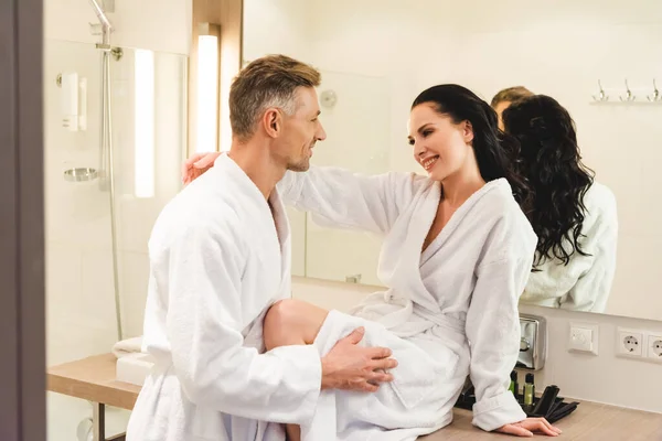 Vue latérale de petit ami souriant et petite amie en peignoirs câlins à l'hôtel — Photo de stock