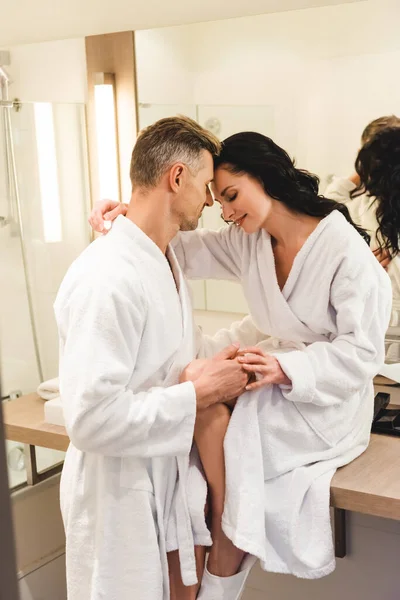 Side view of smiling boyfriend and girlfriend in bathrobes hugging in hotel — Stock Photo