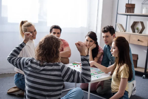 Kiew, Ukraine - 27. Januar 2020: Rückansicht eines Mannes mit Siegergeste in der Nähe unzufriedener Freunde beim Monopoly-Spiel — Stockfoto