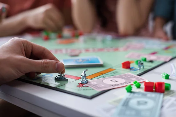 KYIV, UCRANIA - 27 de enero de 2020: vista recortada del hombre sosteniendo la figurilla de juguete mientras juega al juego del monopolio con amigos - foto de stock