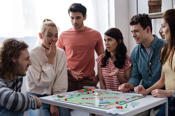 KYIV, UKRAINE - JANEIRO 27, 2020: menina chocada sentada perto de amigos descontentes enquanto joga jogo de monopólio — Fotografia de Stock