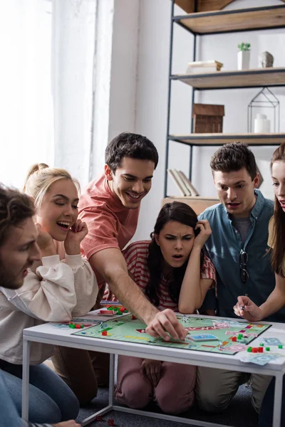 KYIV, UKRAINE - JANEIRO 27, 2020: menina chocada jogando jogo de monopólio com amigos sorridentes — Fotografia de Stock