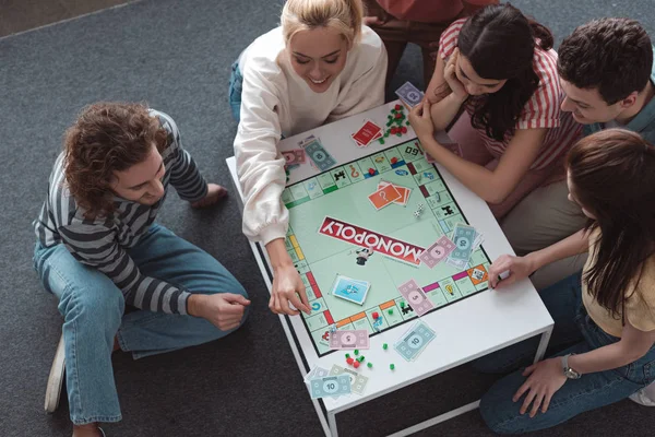 KYIV, UKRAINE - JANUARY 27, 2020: overhead view of smiling friends sitting on floor and playing monopoly game — Stock Photo