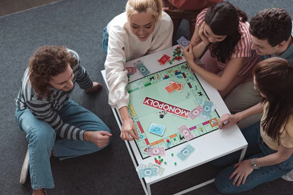 KYIV, UCRANIA - 27 de enero de 2020: vista aérea de amigos sonrientes sentados en el suelo y jugando al juego del monopolio - foto de stock